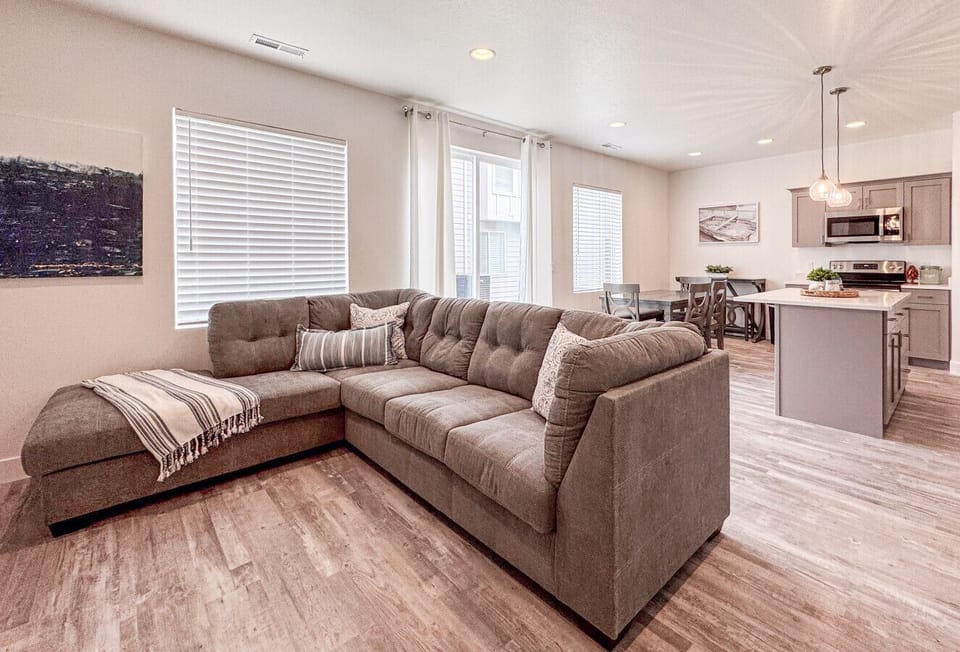 Spacious open-concept living area with cozy sectional, bright windows, and seamless kitchen connection.