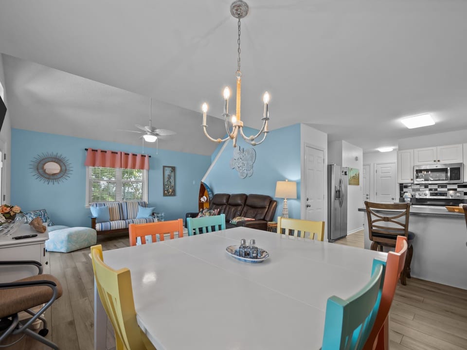 Step into your bright, open living space where colorful dining chairs invite memorable meals and the kitchen awaits your culinary adventures.