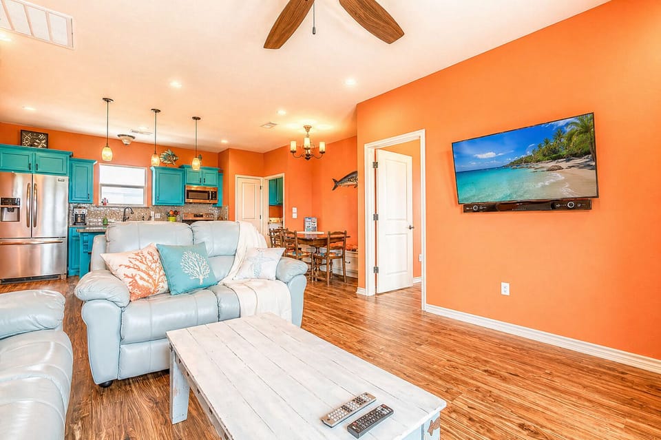 Living room with mounted TV, modern seating, and open layout connecting to dining and kitchen areas.