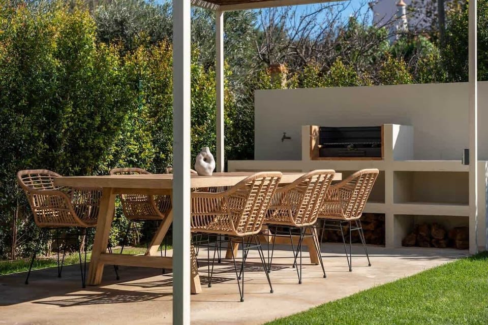 A beautifully designed outdoor dining space featuring a shaded pergola, a built-in grill, and a sink for effortless barbecues. Gather around the elegant dining table for six and enjoy alfresco meals in a serene, nature-filled setting