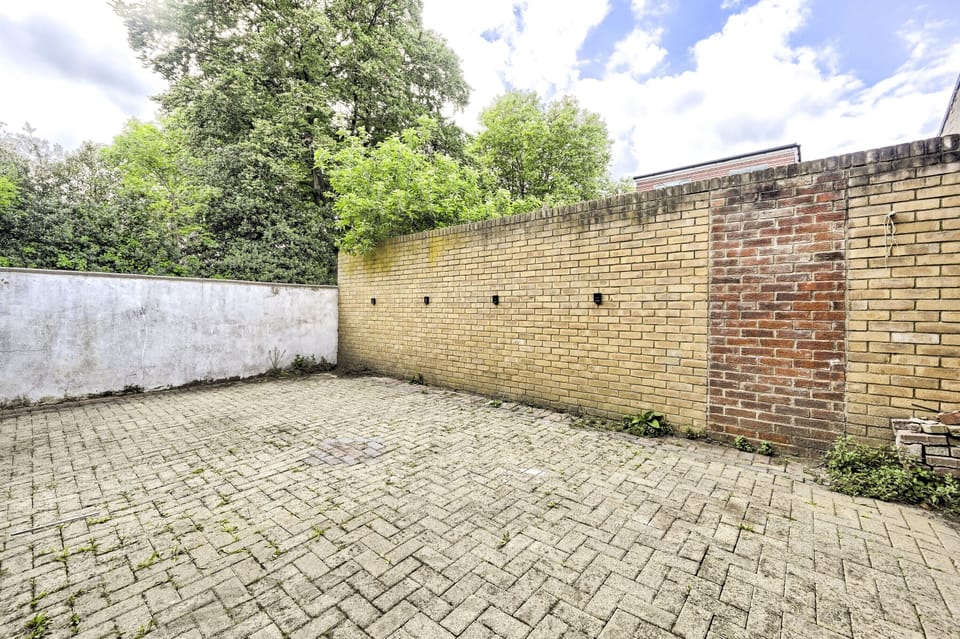 Private walled courtyard, block-paved and fully enclosed, with mature trees beyond the wall