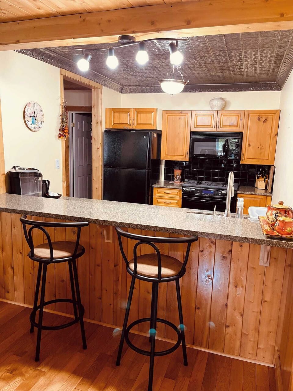 Rustic kitchen with modern lighting, wood finishes, and breakfast bar. Perfect for cozy mornings or evening wine during your cottage stay.