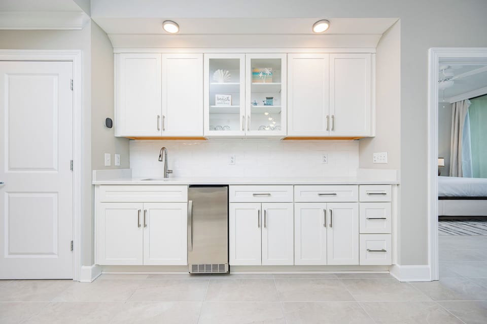Enjoy preparing snacks and drinks in this sleek wet bar, featuring bright cabinetry and glassware display