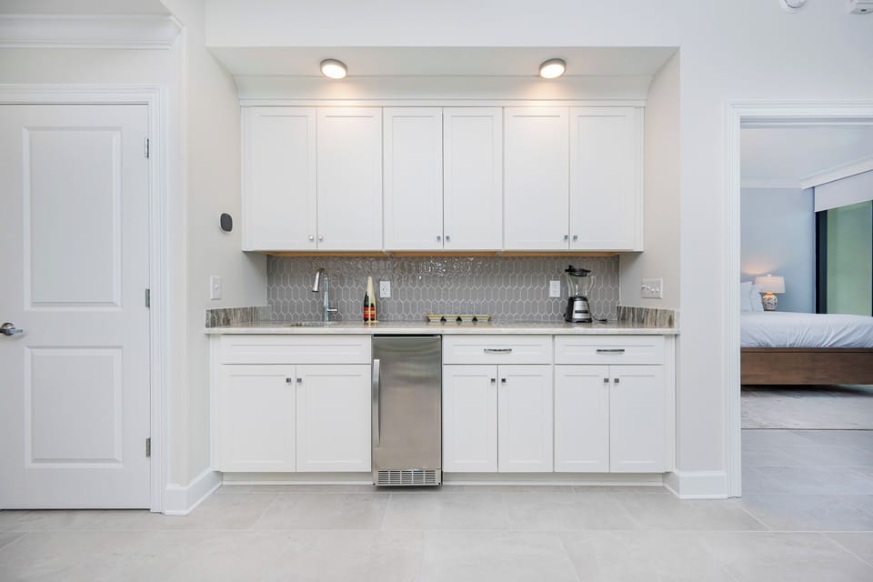 Prepare your favorite drink at the wet bar, featuring stylish cabinetry and elegant backsplash