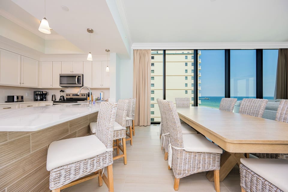 Gather around the large dining table with woven chairs, enjoying views of the beach through expansive windows