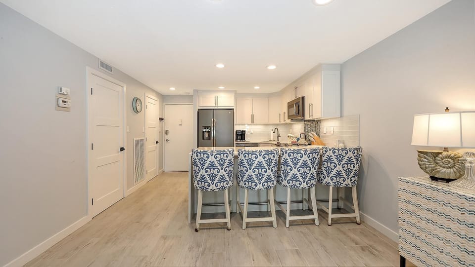 Kitchen with white cabinetry, stainless steel appliances, and four blue-patterned bar stools at the quartz island.