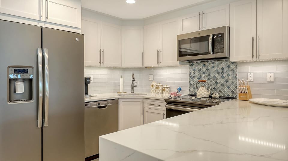 Stainless steel appliances and white cabinetry surround a quartz countertop with marble veining in the kitchen.