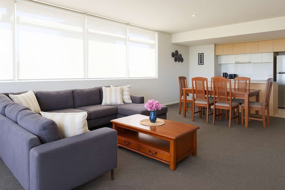 Bright open-plan living and dining area with a comfortable lounge, dining table for six, fully equipped kitchen, and large windows that fill the space with natural light