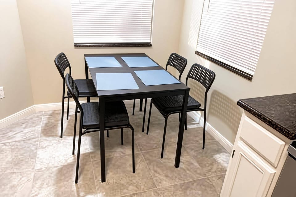 This dining area boasts a sleek black table and six minimalist chairs for comfort. Natural light streams through the shades, enhancing the soft colors and creating a warm, inviting atmosphere for your mealtime experience.