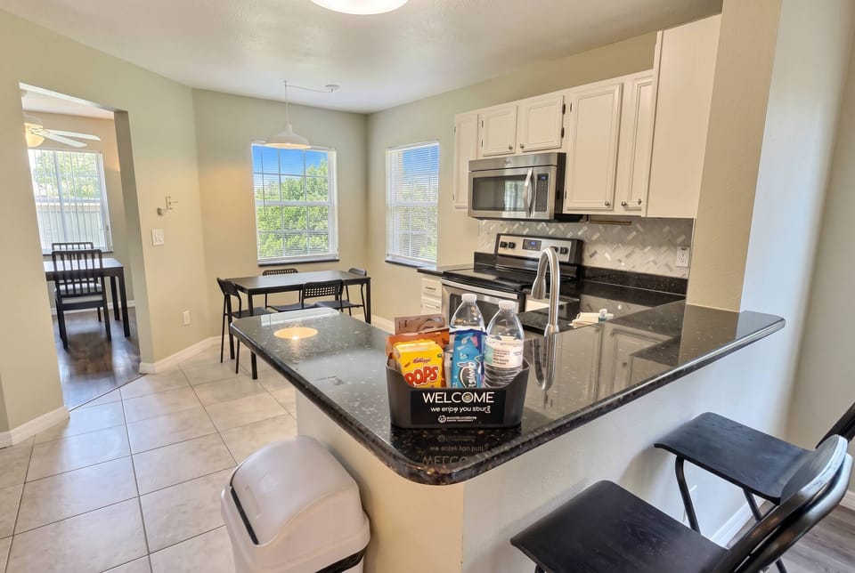 This bright kitchen boasts sleek white cabinetry and a stunning black granite countertop, ideal for meal prep or casual breakfasts. Ample natural light floods in through large windows, creating a warm, inviting atmosphere.