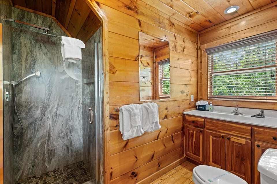Enjoy a refreshing rinse in this modern stone walk-in shower, accented by warm wood walls and natural light.