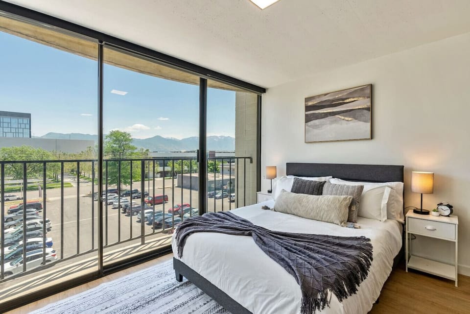 Sunlit bedroom w/ plush bed & sliding doors opening to a private balcony view