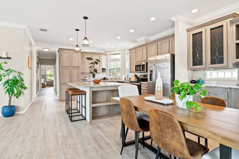 Bright and open kitchen and dining area features a large island with bar stools and a wooden dining table, perfect for family meals.

