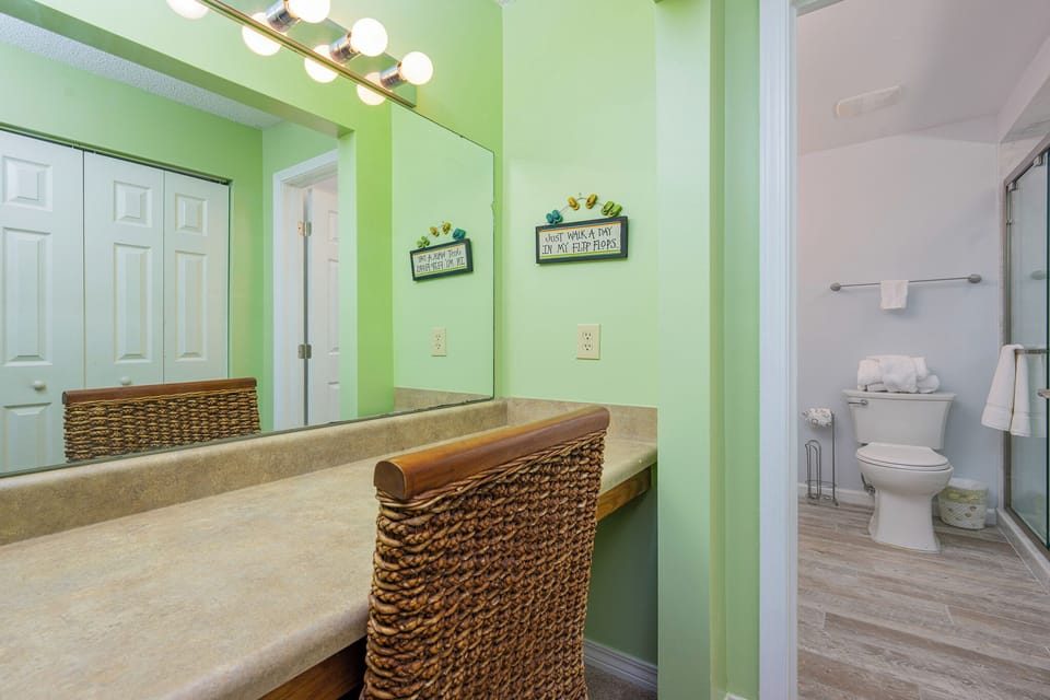 The master bathroom features a vibrant green color scheme, a spacious vanity with a woven stool, and a glass-enclosed shower