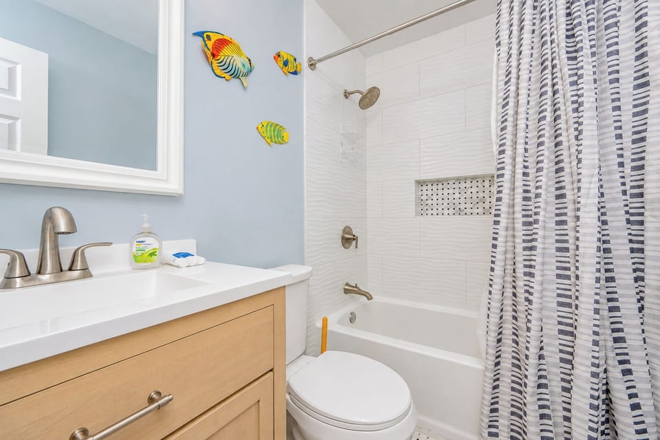 This guest bathroom features a stylish vanity with a sleek sink, vibrant fish decor, and a relaxing shower-tub combo