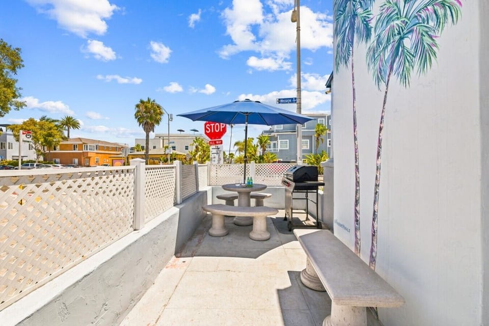 Private fenced patio with a gas grill, bistro table, and hand-painted palm mural — an inviting spot for an outdoor meal.