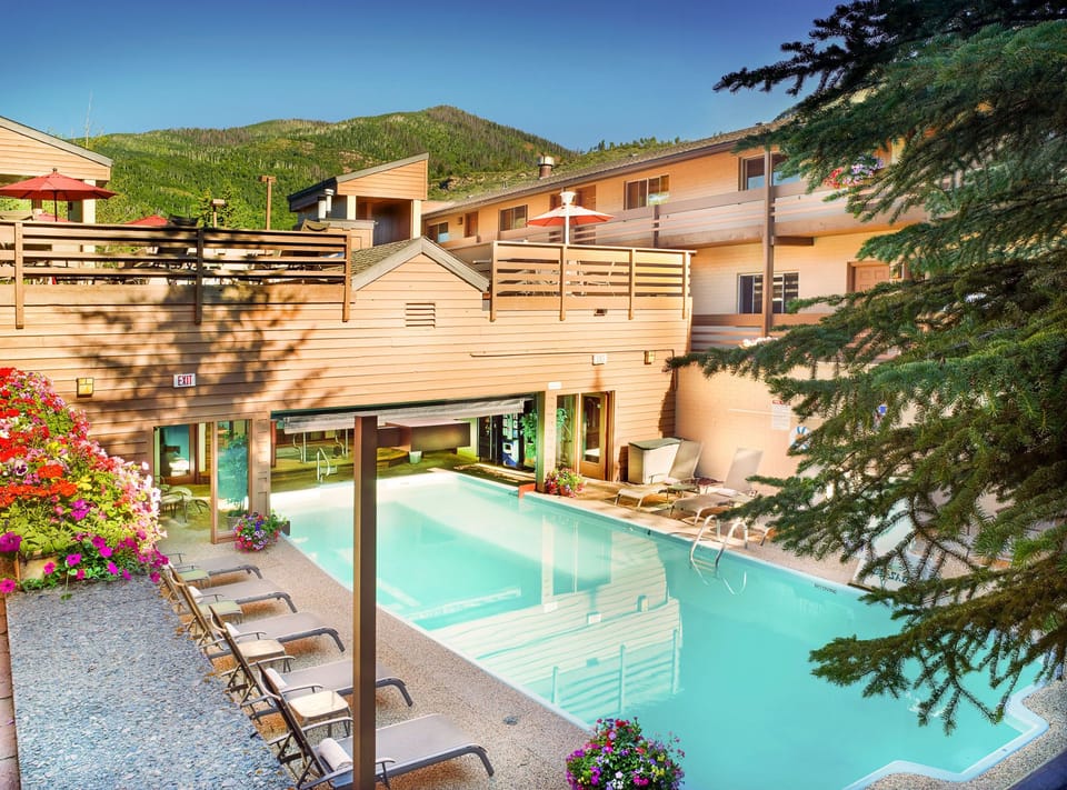 Dive into the refreshing shared pool surrounded by lush flowers and comfortable lounge chairs, perfect for soaking up the sun against a stunning mountain backdrop.