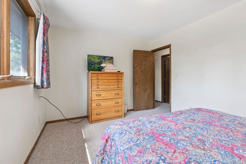 Another angle of the bedroom showing colorful bedding and a dresser for storage.