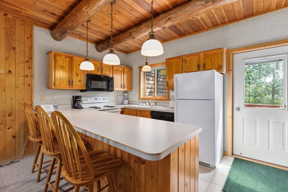 Cabin kitchen with wood cabinetry, bar seating, and full appliances.