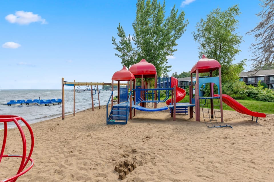 Sandy playground with slides and climbing equipment by the water.