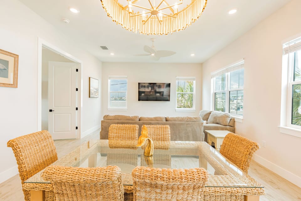 Chic dining room featuring a glass-top table, wicker chairs, and a rustic wooden chandelier—blending coastal charm with effortless elegance.