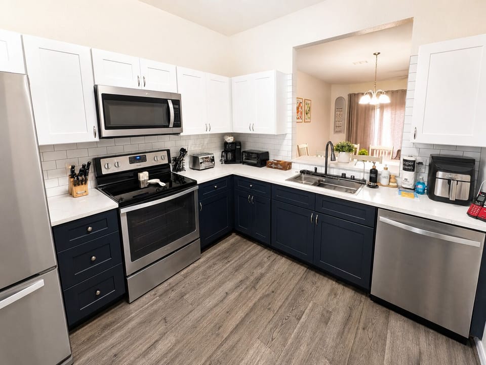Fully equipped modern kitchen with stainless steel appliances, white cabinetry, navy lower cabinets, coffee station, and open view to the dining area — perfect for preparing meals during your Regal Palms stay.