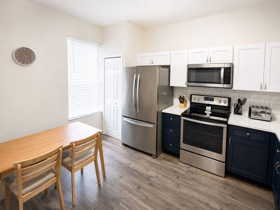 Bright eat-in kitchen with stainless steel appliances, full-size refrigerator, oven, microwave, and a cozy breakfast table — perfect for quick meals, snacks, and family mornings before heading to the parks.
