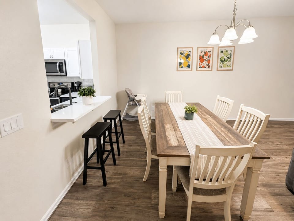Spacious dining area with seating for six, breakfast bar stools, and an open view into the kitchen — perfect for family meals, game nights, and gathering after a day at the parks.