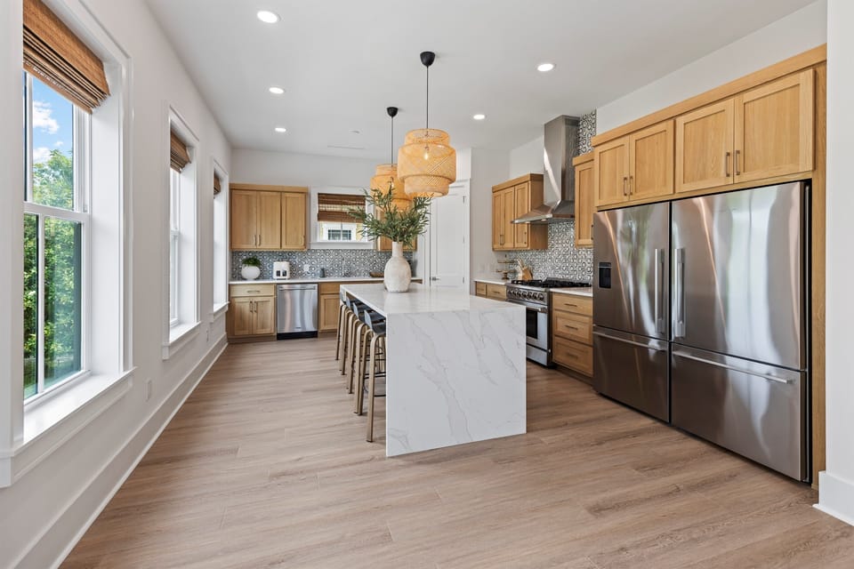 Your modern kitchen features warm wood cabinets, marble island seating, and stainless appliances bathed in natural light.