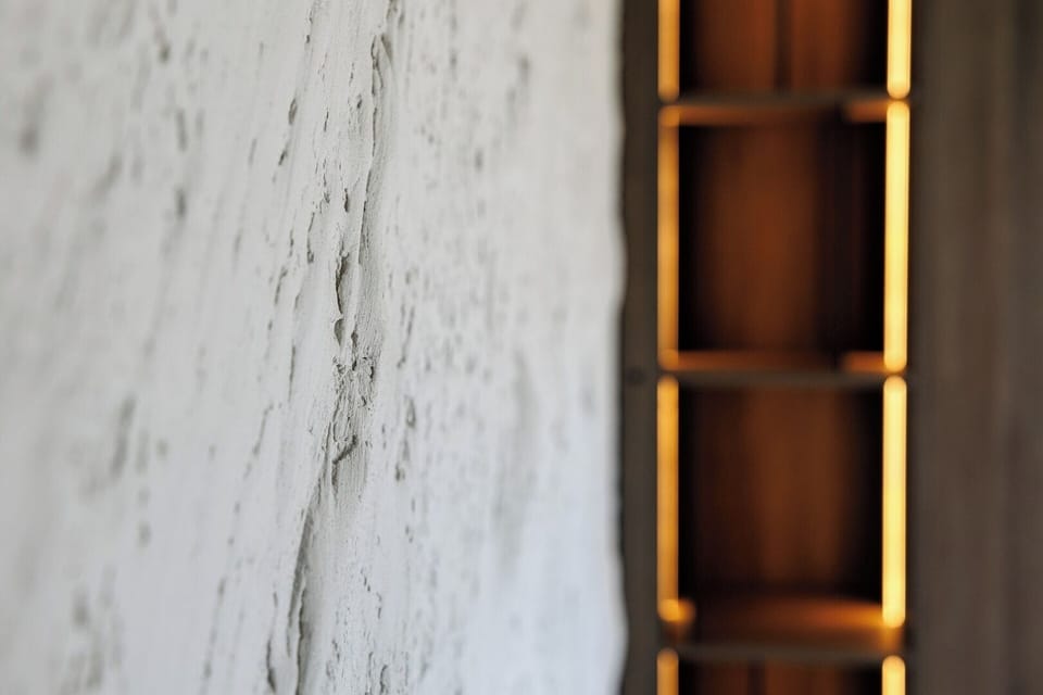 Close-up of the handcrafted plaster wall, softly lit to highlight its organic texture. Paired with warm wood shelves, it adds earthy elegance and a rustic-luxe vibe to the living space.