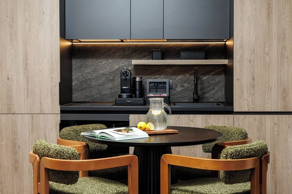 Sleek black kitchen with marble backsplash, espresso machine, toaster, and dining set—fully equipped for gourmet mornings or quick bites.