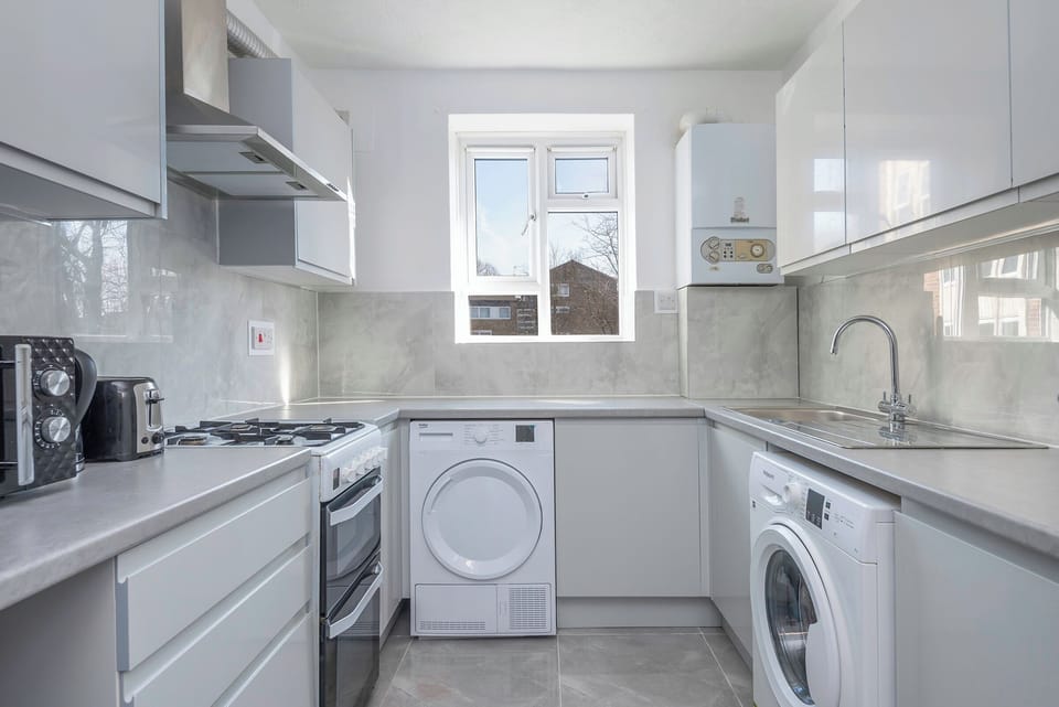 Modern kitchen with grey cabinets, washer/dryer, and bright window light.