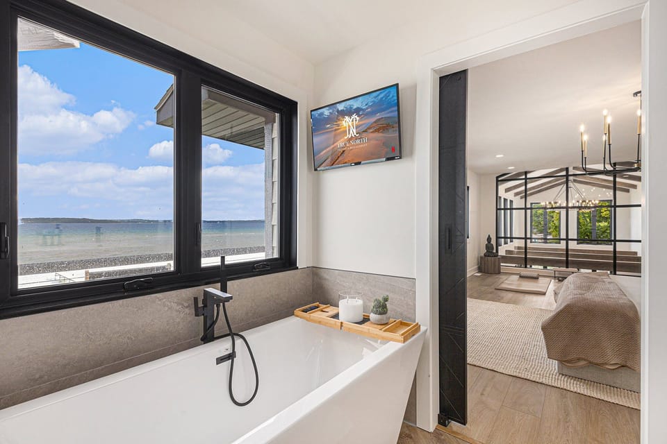 Freestanding white bathtub beneath a large window overlooking the bay.