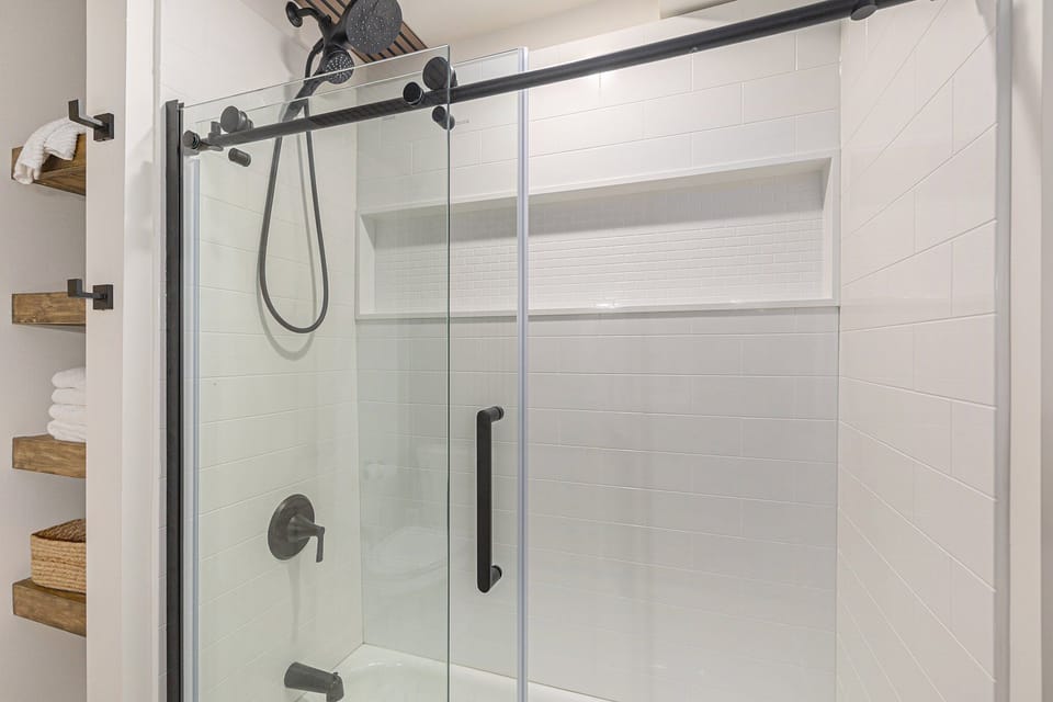 Tub and shower with black-framed sliding glass doors and handheld showerhead.