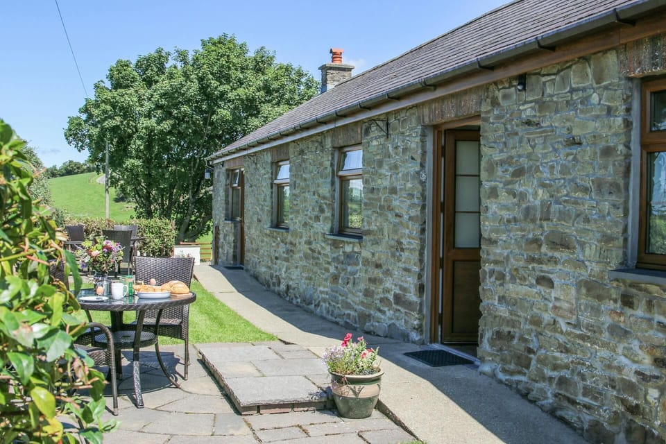 Outside view of Y Dderwen cottage, patio with small table and chairs, front door