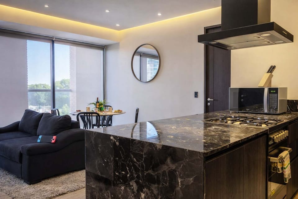 Living room w/ plush seating beside a marble kitchen island & modern lighting