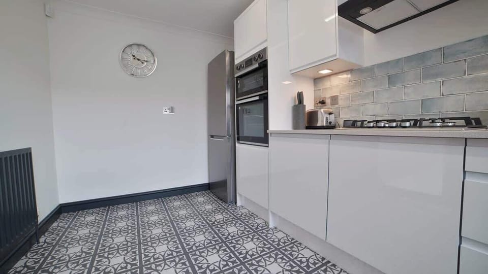 Sleek and modern full kitchen featuring glossy white cabinets, built-in double ovens, a gas cooktop, washing machine, and patterned tile flooring—designed for both style and functionality.