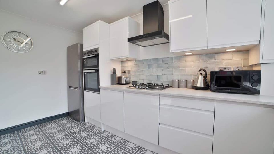 Sleek and modern full kitchen featuring glossy white cabinets, built-in double ovens, a gas cooktop, washing machine, and patterned tile flooring—designed for both style and functionality.