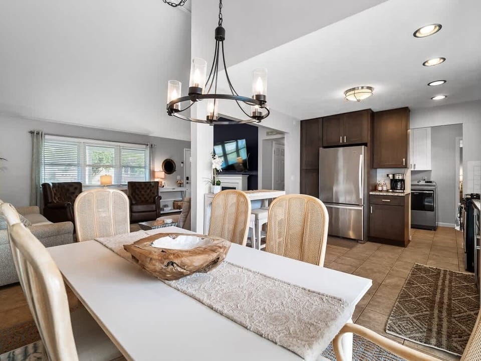 Elegant dining space with seating for six ️, set beneath a statement chandelier . Natural light flows in through sheer curtains, creating a bright and welcoming area for meals, games, or conversation .