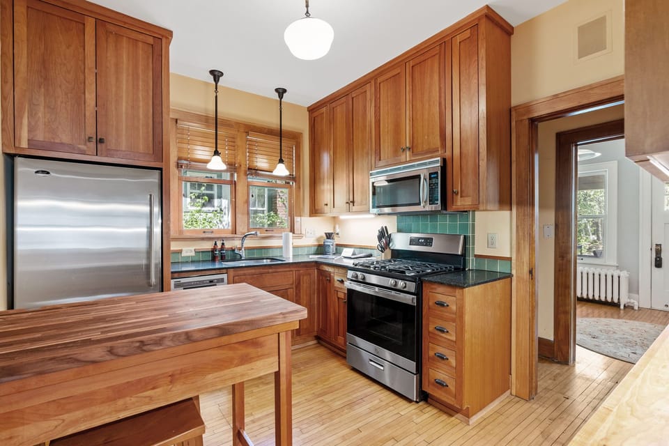 Your warm wooden kitchen invites culinary adventures with modern appliances, granite counters, and charming green tile backsplash creating the perfect cooking space.