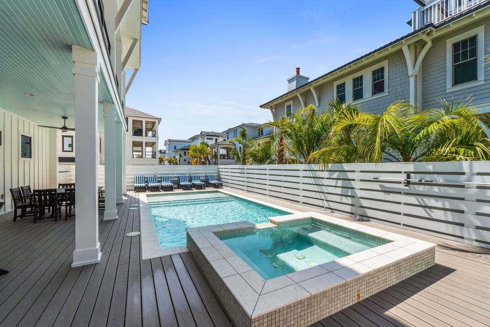 A coastal-style property featuring a private pool and spa with modern horizontal fencing, surrounded by tropical palms and beach-inspired architecture.