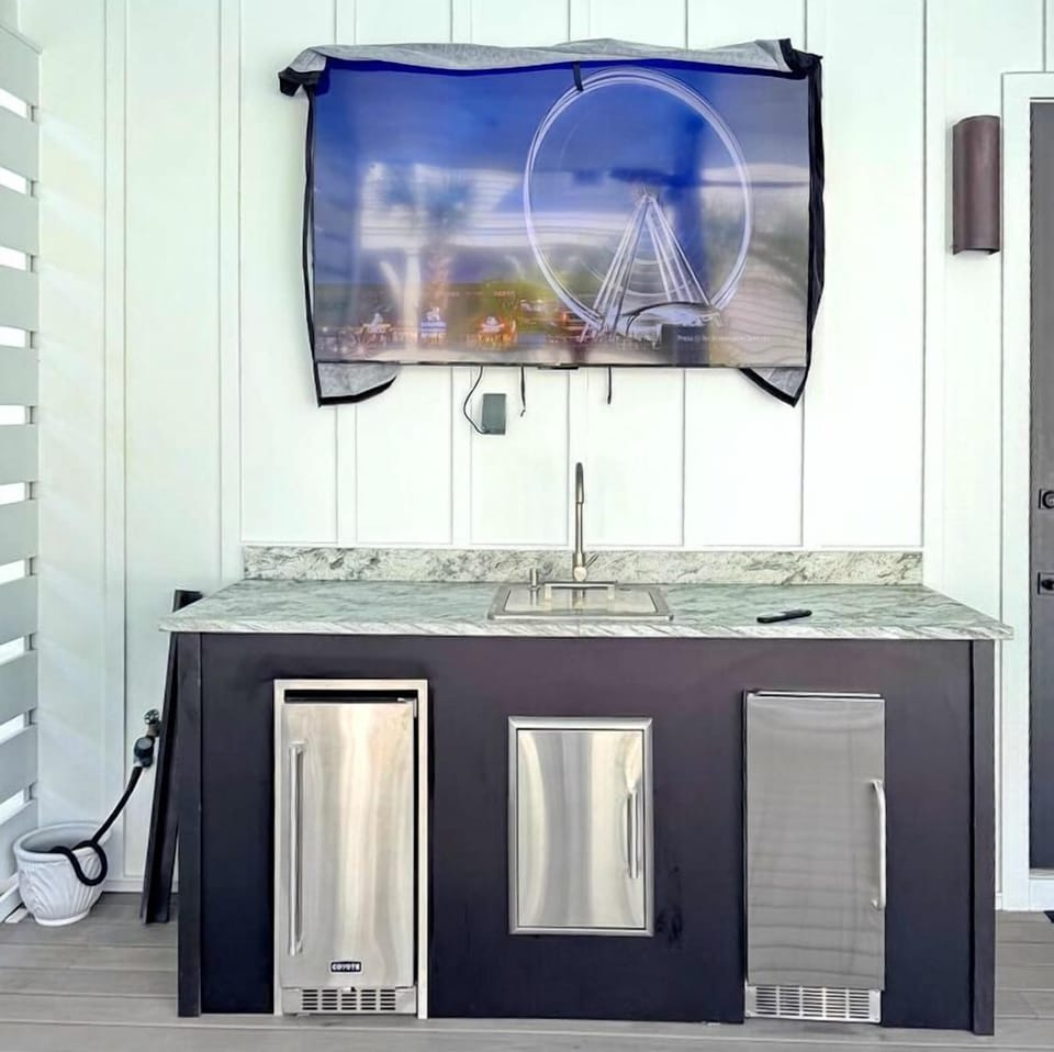 Modern outdoor wet bar features sleek granite countertop, stainless appliances, and sink, perfect for entertaining under the coastal artwork.