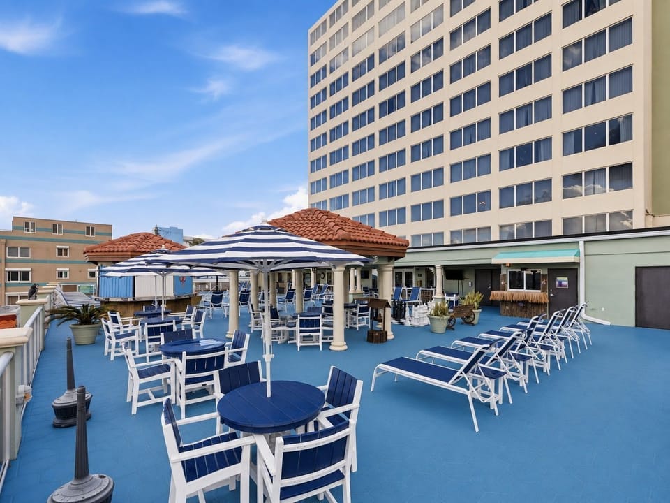 Rooftop terrace with tables, umbrellas, and lounge chairs, overlooking buildings