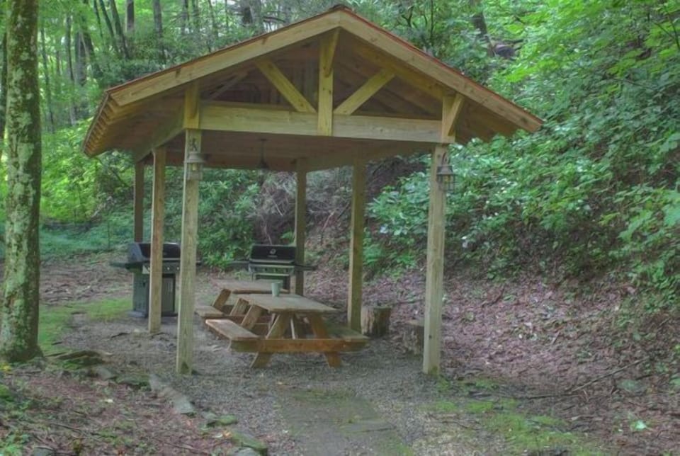 Enjoy outdoor cooking in this serene shared BBQ area, surrounded by lush greenery, with ample seating for gatherings.
