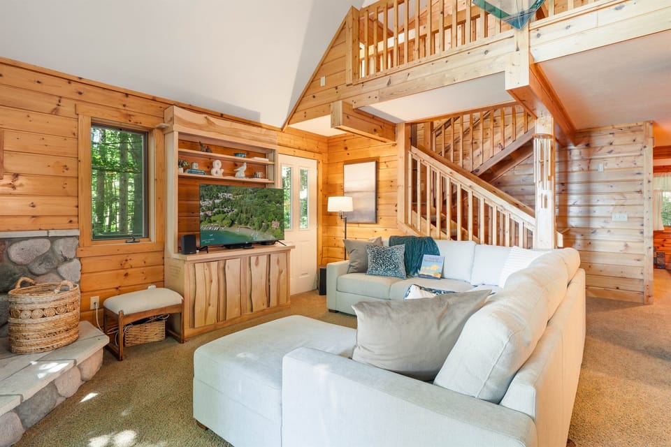 This cozy A-frame lakehouse living room features a plush sectional sofa facing panoramic floor-to-ceiling windows with stunning lake views.