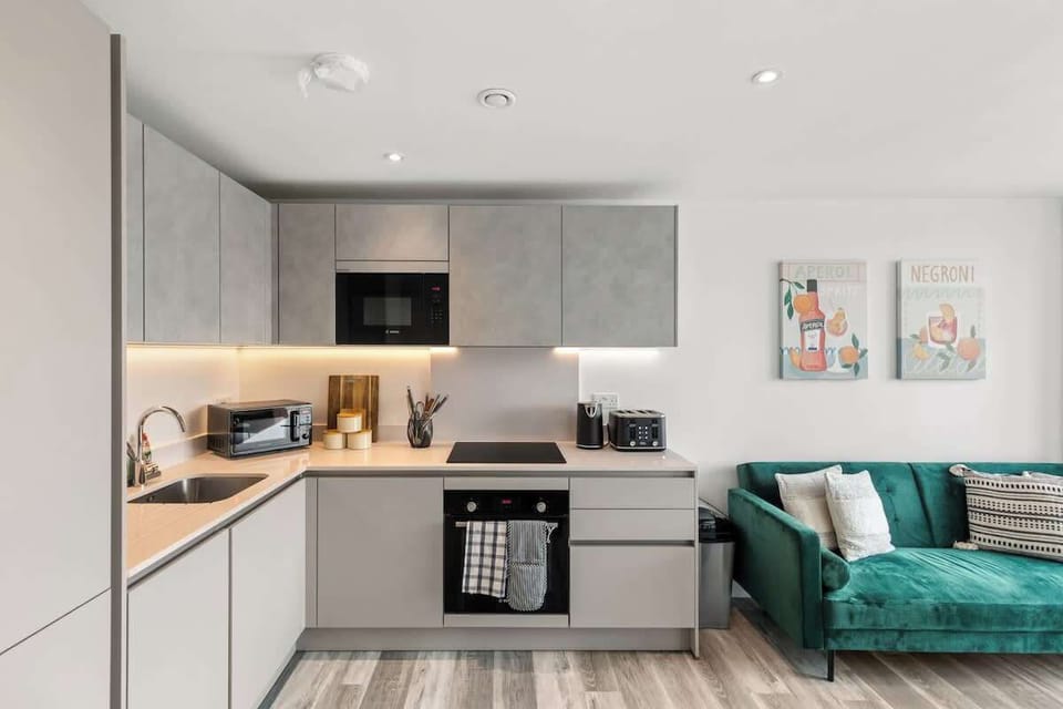 - Modern kitchen with built-in appliances and sleek cabinets  
- Open-plan layout connects kitchen to cozy green sofa space  
- Airbnb apartment designed for comfort and convenience  