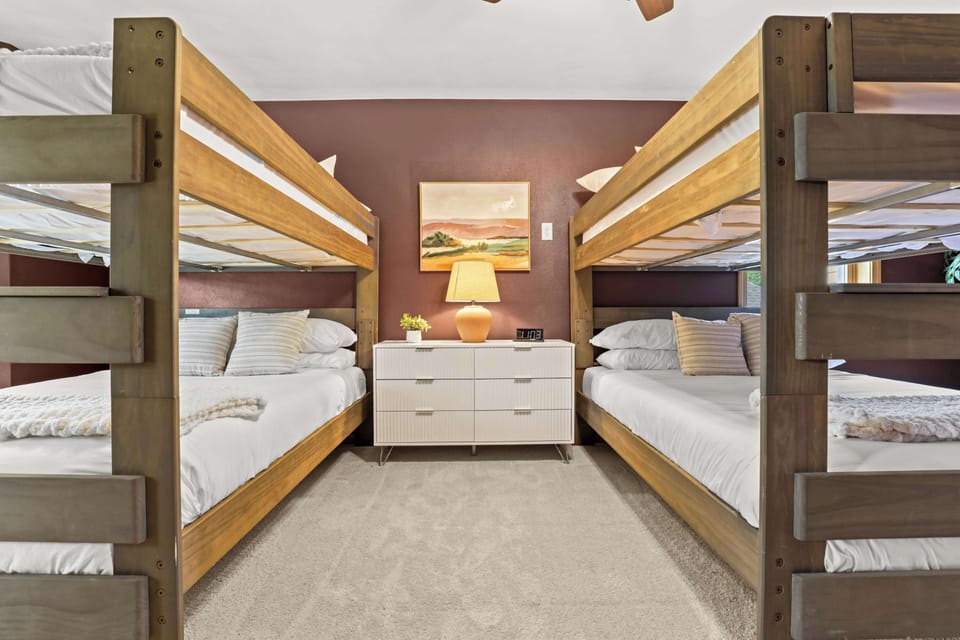 Bedroom 5 - large bedroom upstairs featuring 4 queen beds, connected master suite bathroom, 58" smart tv, dedicated workspace, ceiling fan, two mobile fans, and a phone charging station.