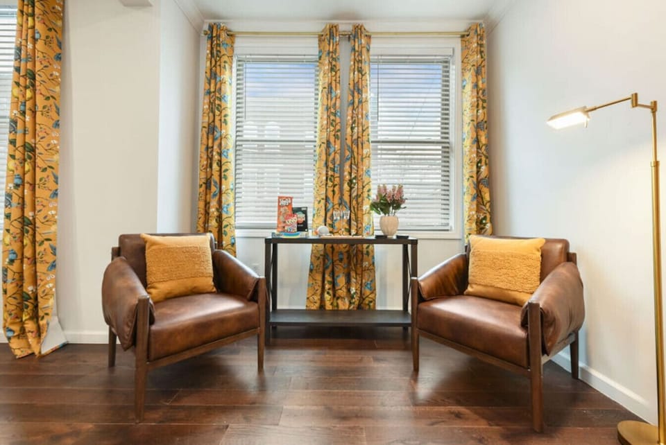 A comfortable seating nook with warm leather chairs and vibrant floral curtains, perfect for relaxing or reading.