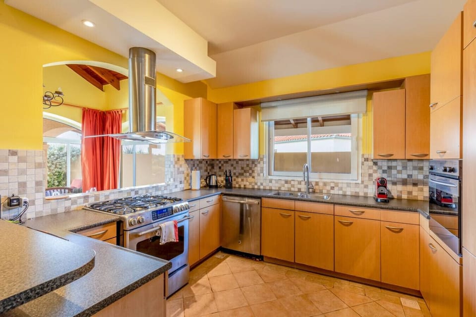 Modern kitchen with sleek wood cabinetry, a gas stove, and stainless steel appliances. Features a spacious countertop, mosaic tile backsplash, and ample natural light through large windows, creating a bright and functional cooking space.