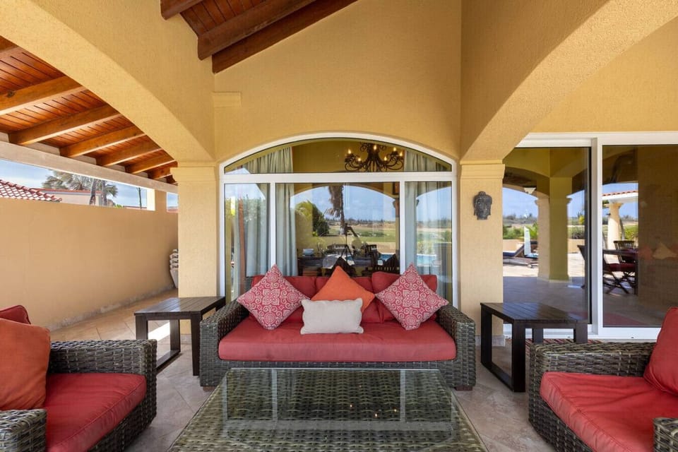 Spacious patio with comfortable wicker seating, bright red cushions, and a glass coffee table. Ideal for relaxing and enjoying the outdoor view, with a peaceful atmosphere under a high, arched ceiling.